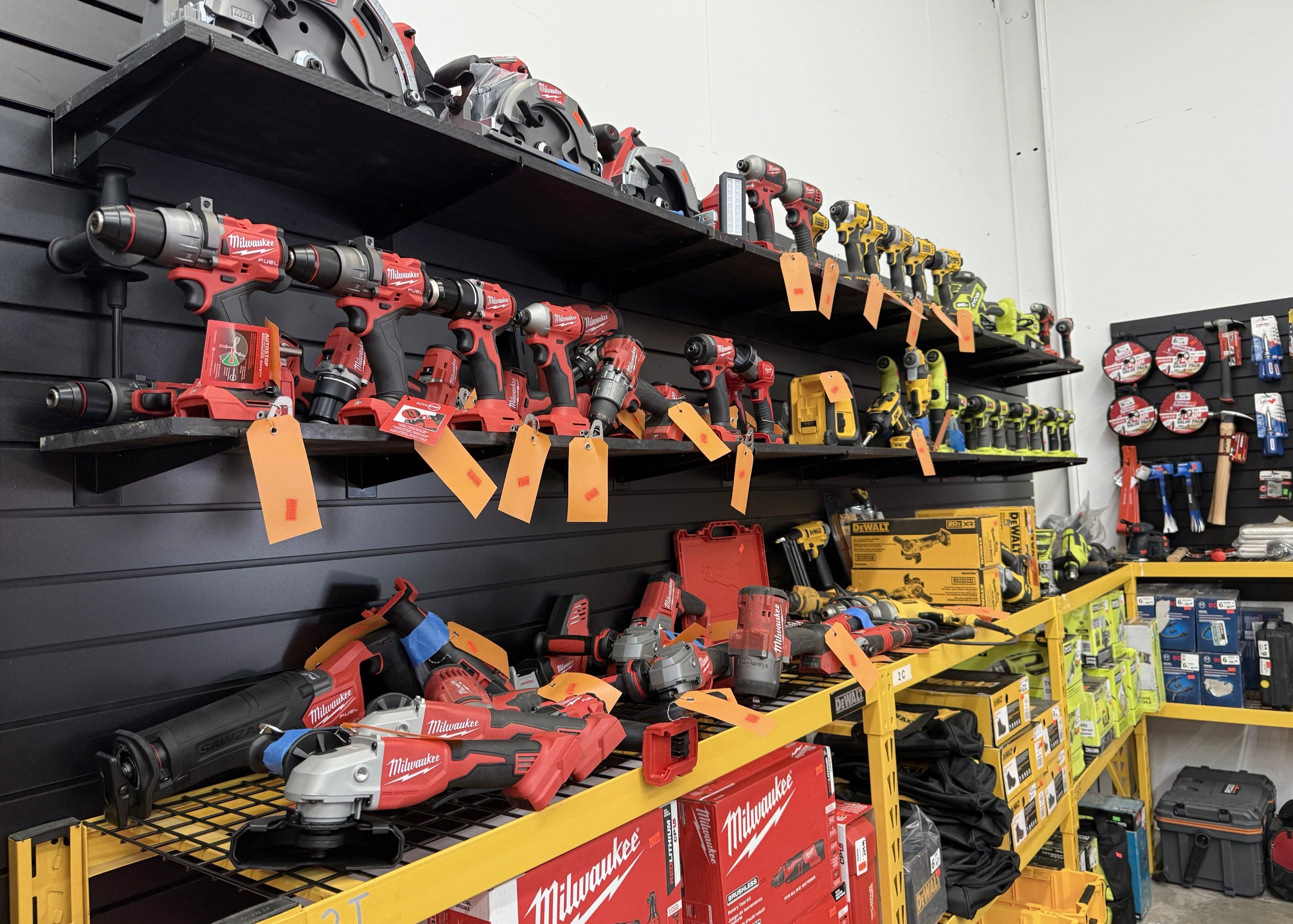Wall display of power tools including Ryobi, Ridgid, and Milwaukee drills and saws, organized on shelves at MTP Liquidations warehouse in Raleigh, NC