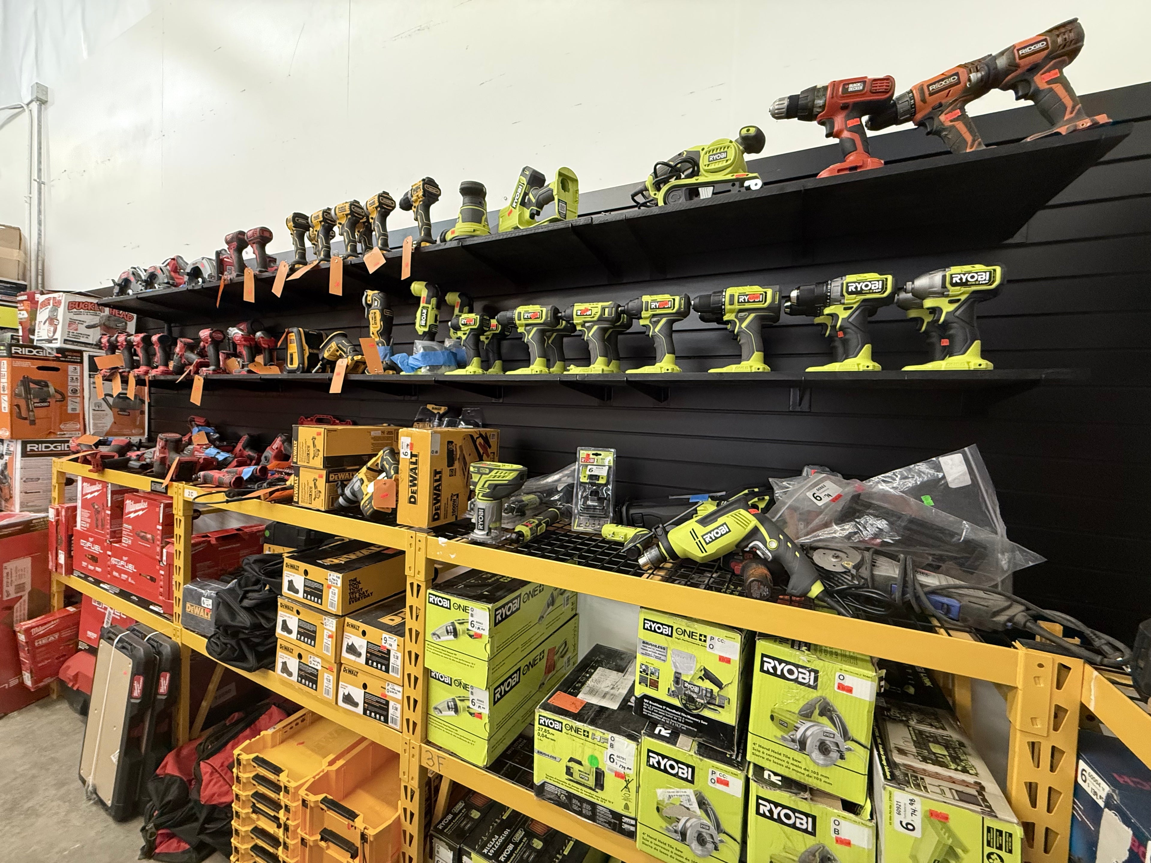 Wall display of power tools including Ryobi, Ridgid, and Milwaukee drills and saws, organized on shelves at MTP Liquidations warehouse in Raleigh, NC